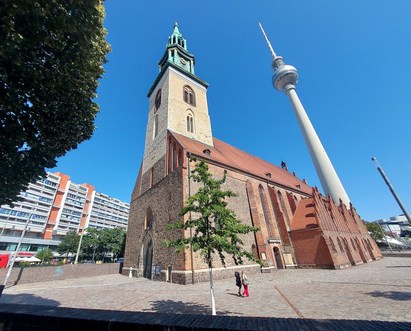 Die Backsteinkirche St. Marien mit grünem Turmhelm, hinter der der Fernsehturm in den klaren Himmel ragt