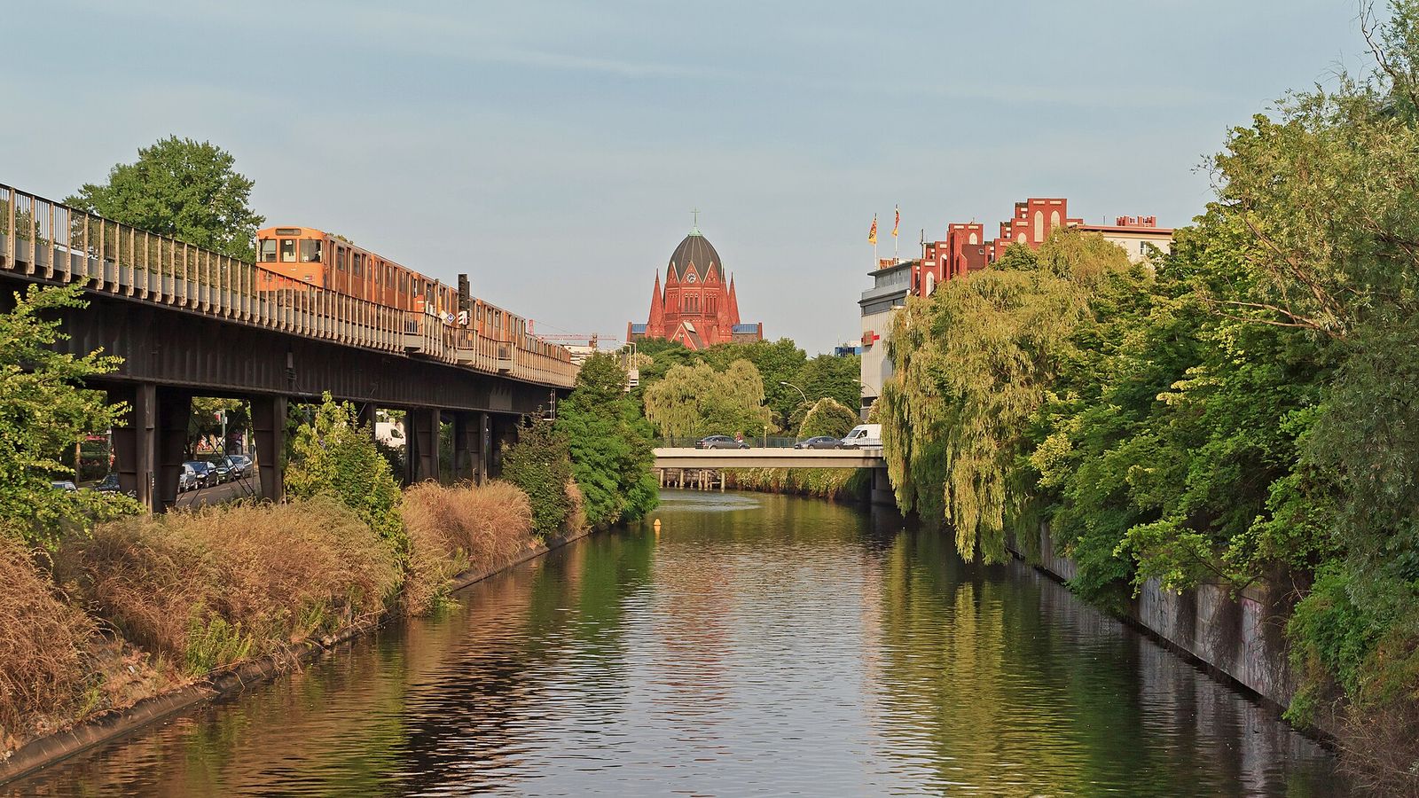 Der Landwehrkanal in Kreuzberg mit der Hochbahn auf dem Viadukt links, Trauerweiden am Ufer rechts und einer roten Backsteinkirche im Hintergrund