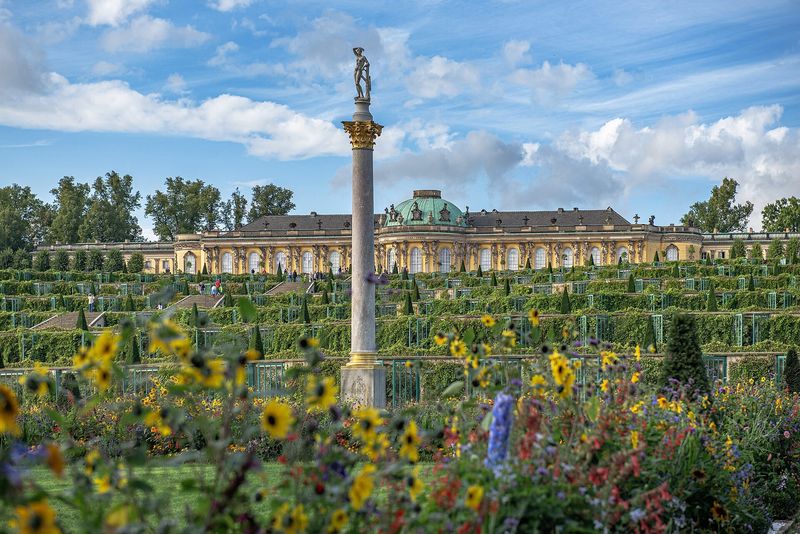 Schloss Sanssouci über den Weinbergterrassen in Potsdam, im Vordergrund Sommerblumen und eine Säule mit Statue